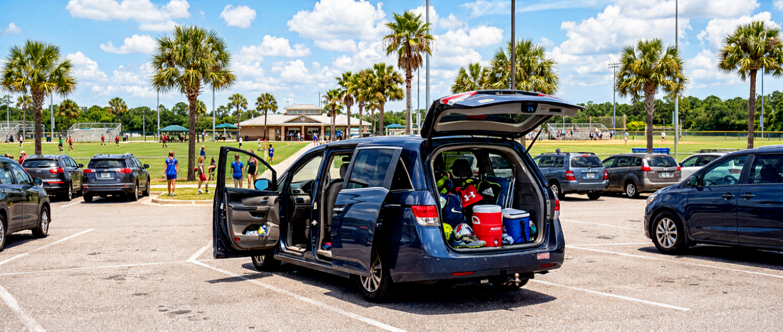 Used Honda Odyssey minivan with cargo doors open at a Florida sports complex parking lot, sports gear loaded inside