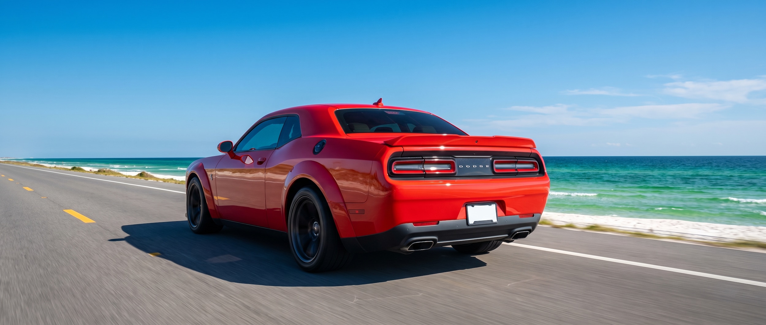 A red Dodge Challenger driving along a coastal highway with emerald Gulf water visible in the background, sunny Florida Panhandle afternoon sky, photographed from a low rear-three-quarter angle to show the wide muscle-car stance