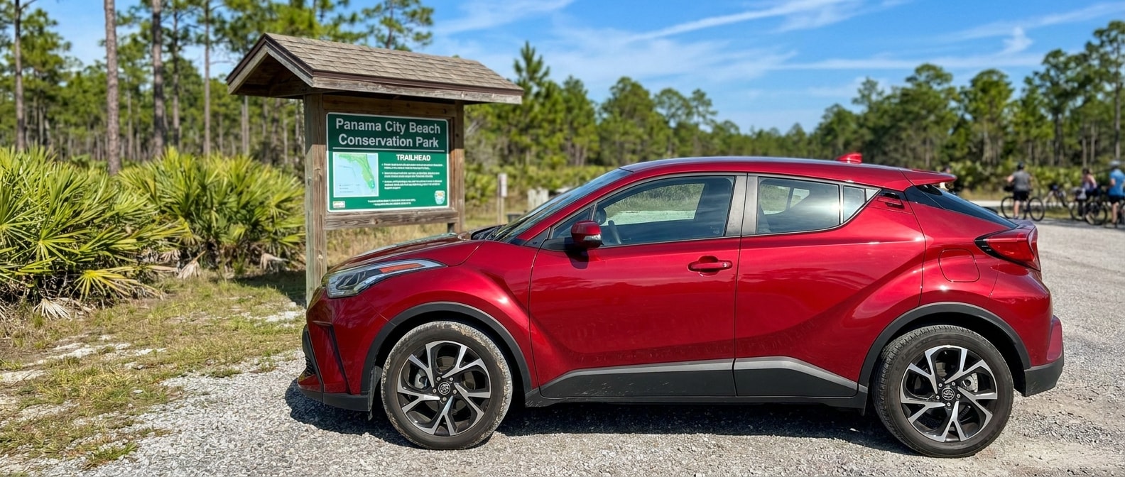 A used 2021 or 2022 Toyota C-HR in a bold color (red or blue) parked on a sunny Gulf Coast day, with pine flatwoods or a park trailhead in the soft background. This represents the Panama City Beach Conservation Park area lifestyle with compact crossover profile clearly visible and Florida sky overhead.