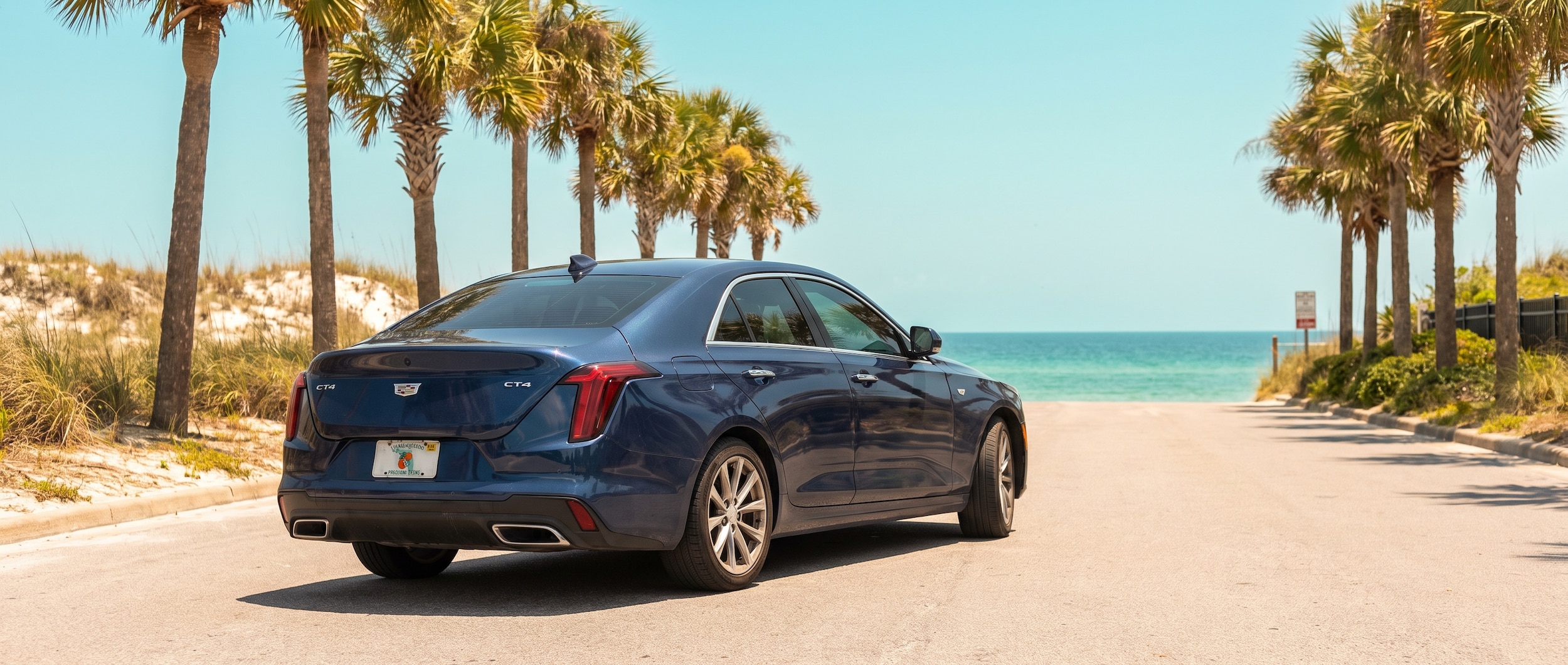 A used Cadillac CT4 sedan in a deep dark metallic finish parked on a sun-drenched coastal boulevard near Panama City Beach, Florida, with palm trees and bright Gulf sky in the background, summer 2026.