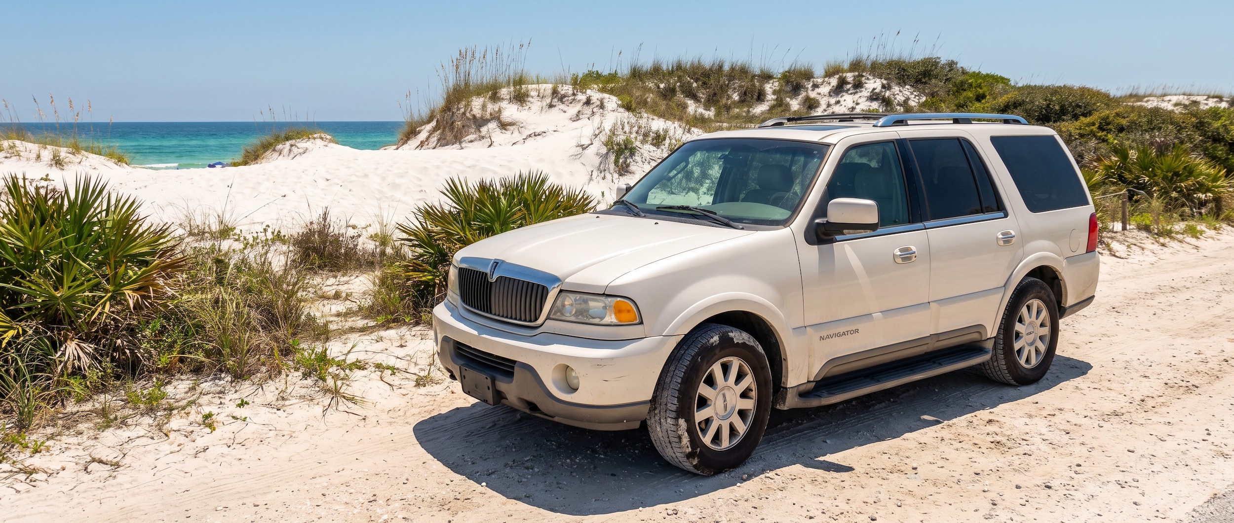 A used Lincoln Navigator in Pearl White or Black parked near sugar-white sand dunes with coastal scrub vegetation, Walton County Florida beach access, bright July sunshine, Gulf of Mexico emerald water visible in the background, 2026 model year styling cues