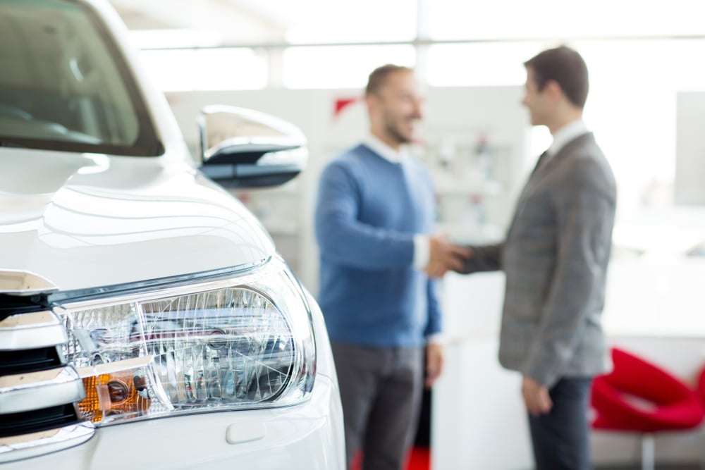 Up-close view of a vehicle headlight with two people shaking hands in the background Up-close view of a vehicle headlight with two people shaking hands in the background