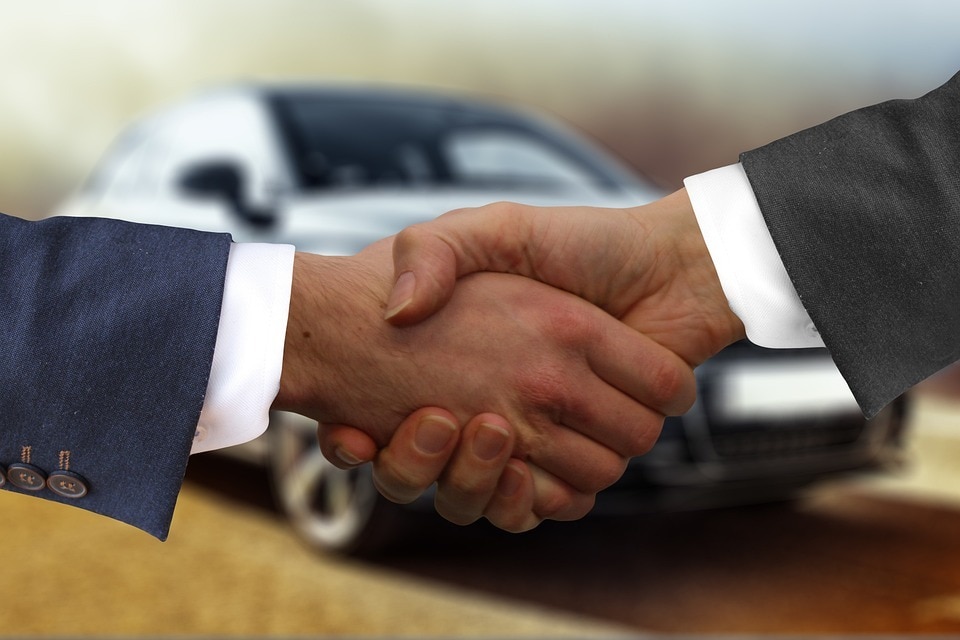  two people shaking hands after completing a car sale