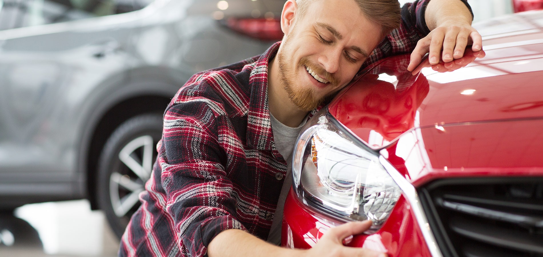Smiling man hugs the hood of his used car