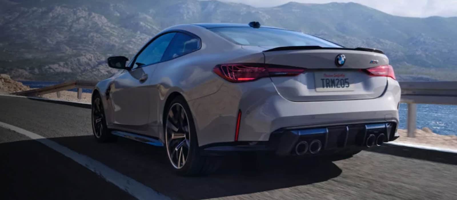 A white 2026 BMW 4 Series Coupe driving by the water, with mountains in the background