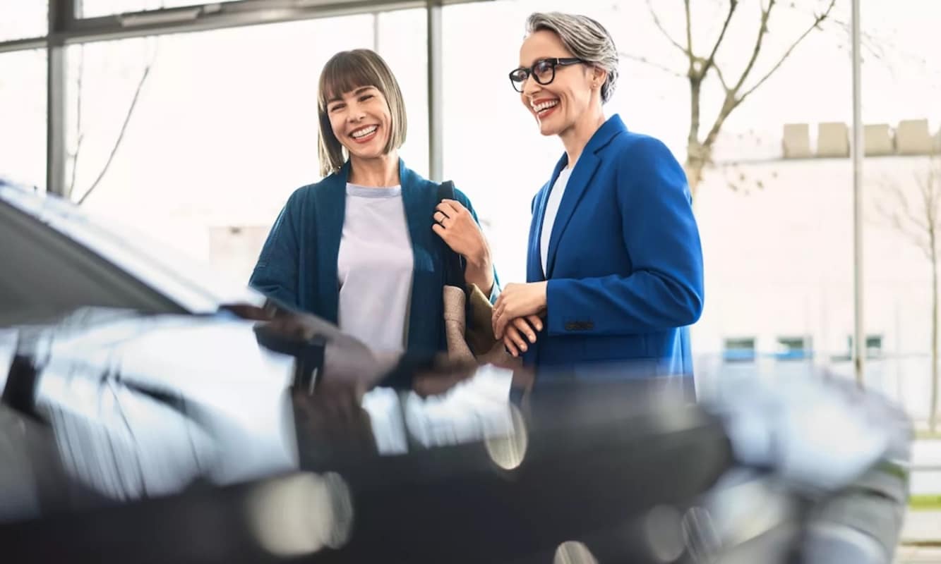 Two women smiling at a car inside a car dealership