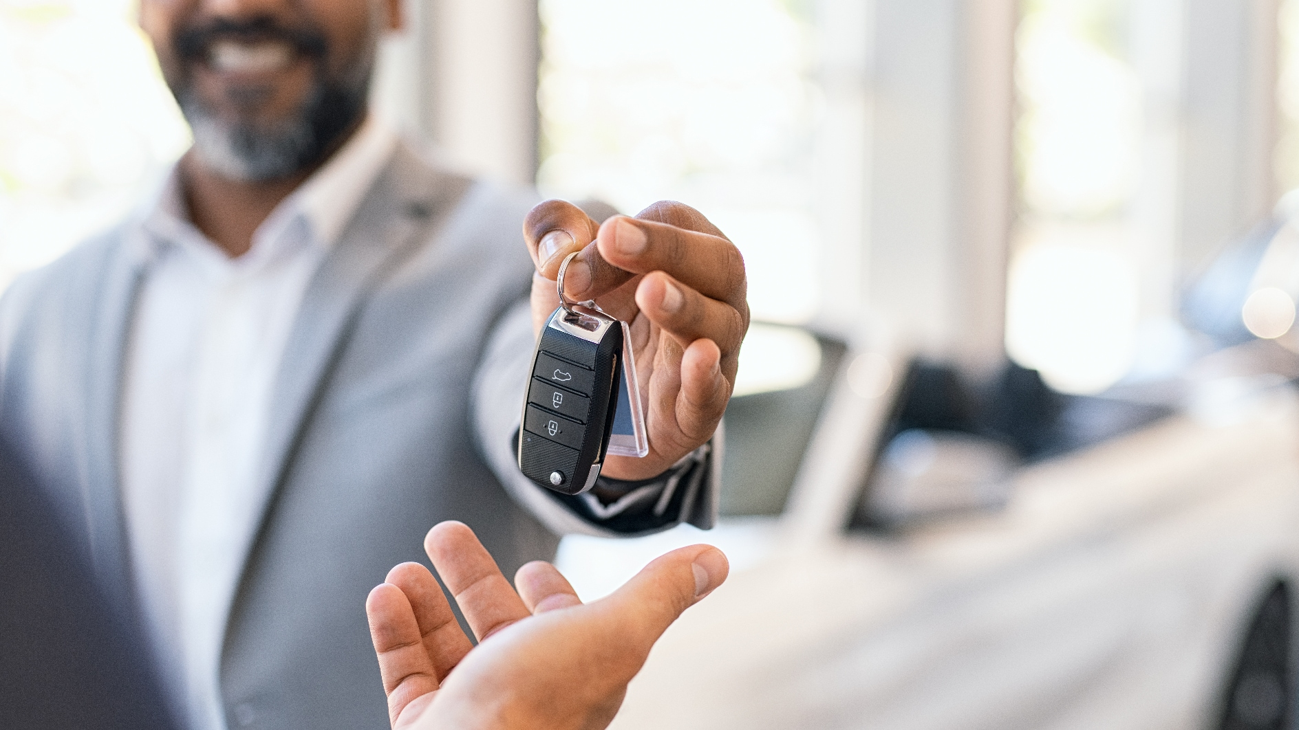 A car salesman handing a customer a car key inside a car dealership