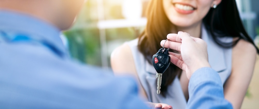 A car dealer handing a smiling woman a car key