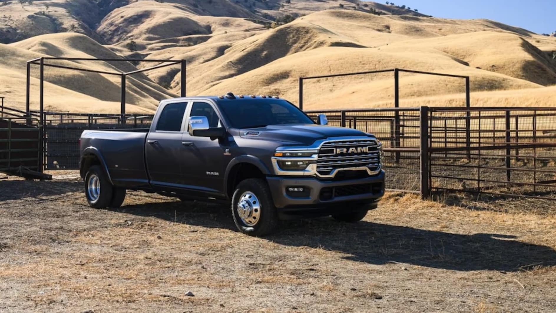 A gray 2026 Ram 3500 truck parked in front of a paddock with dry grass hills in the background