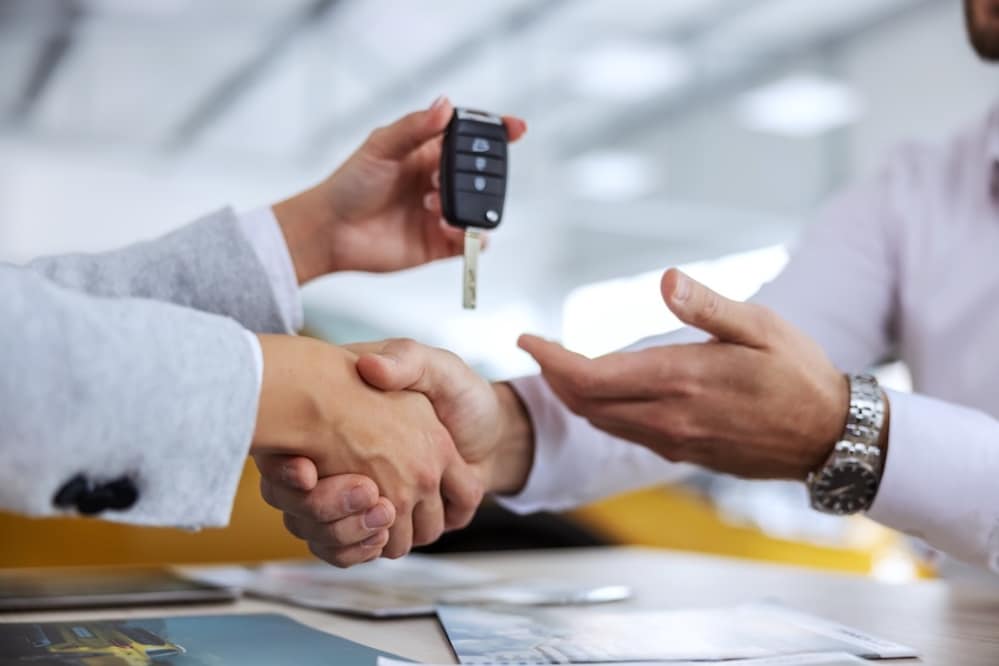 A car dealer shaking hands and giving a car key to a customer