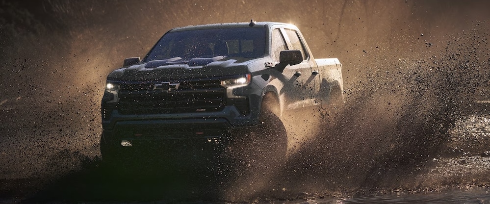 A dark-colored 2026 Chevrolet Silverado truck splashing through mud
