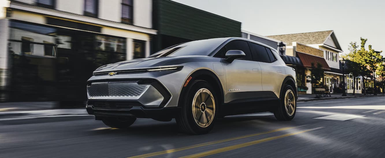A silver 2026 Chevy Equinox EV driving down a small-town commercial street