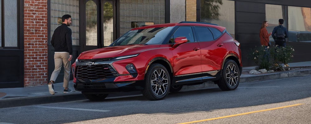 A man walking beside a red 2026 Chevrolet Blazer SUV parked on a city street