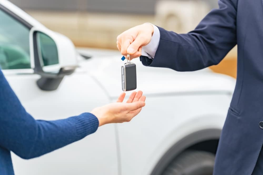 A car dealer handing a customer a car key in front of a white vehicle