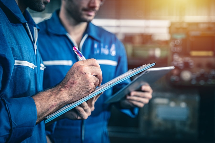 Two service technicians in blue coveralls looking at a clipboard inside a service center