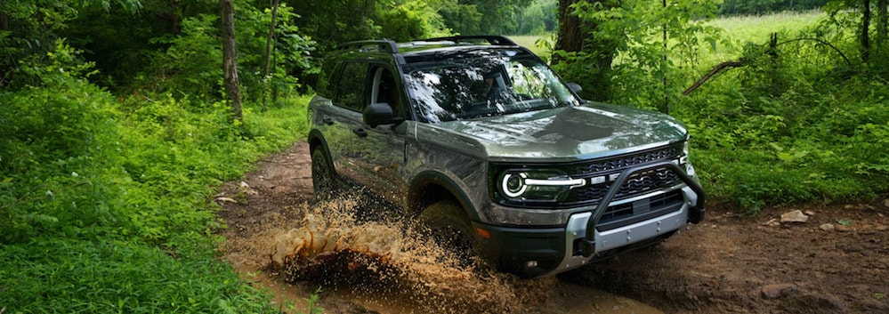 A gray 2026 Ford Bronco splashing through standing water on a muddy road