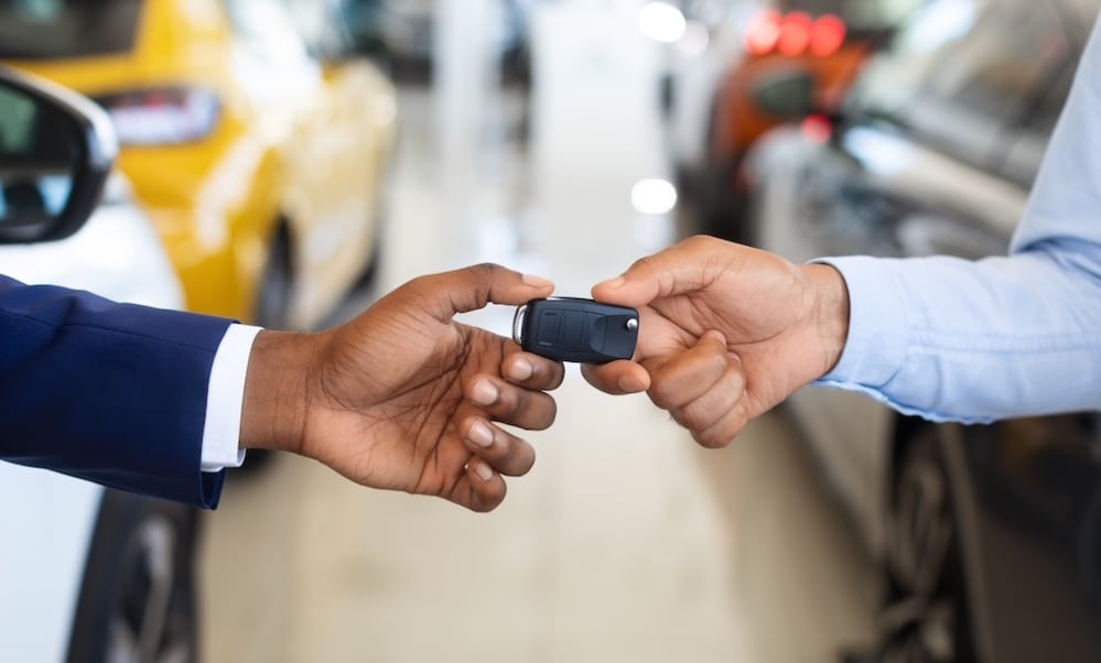 A car dealer handing a customer a car key inside a dealership