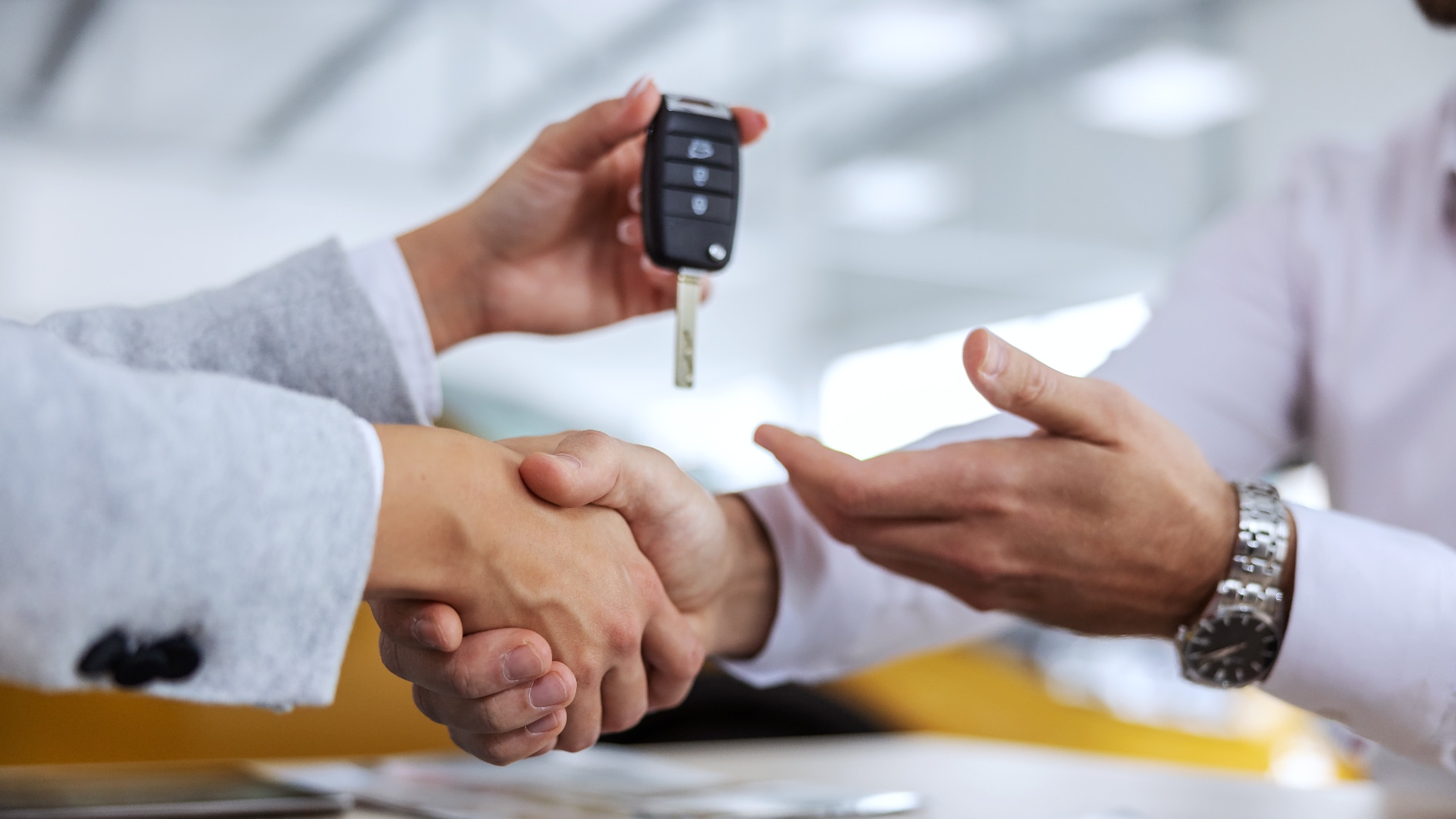 A car salesman shaking hands with a customer and handing over a key fob