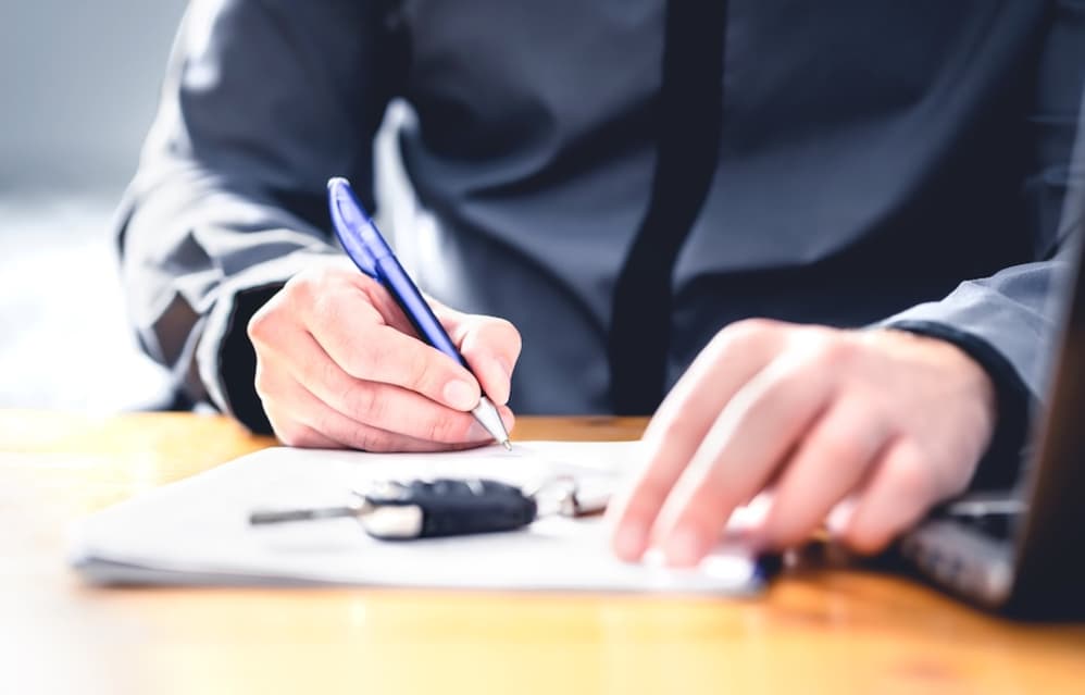 A customer signing paperwork on a clipboard, with a car key in hand