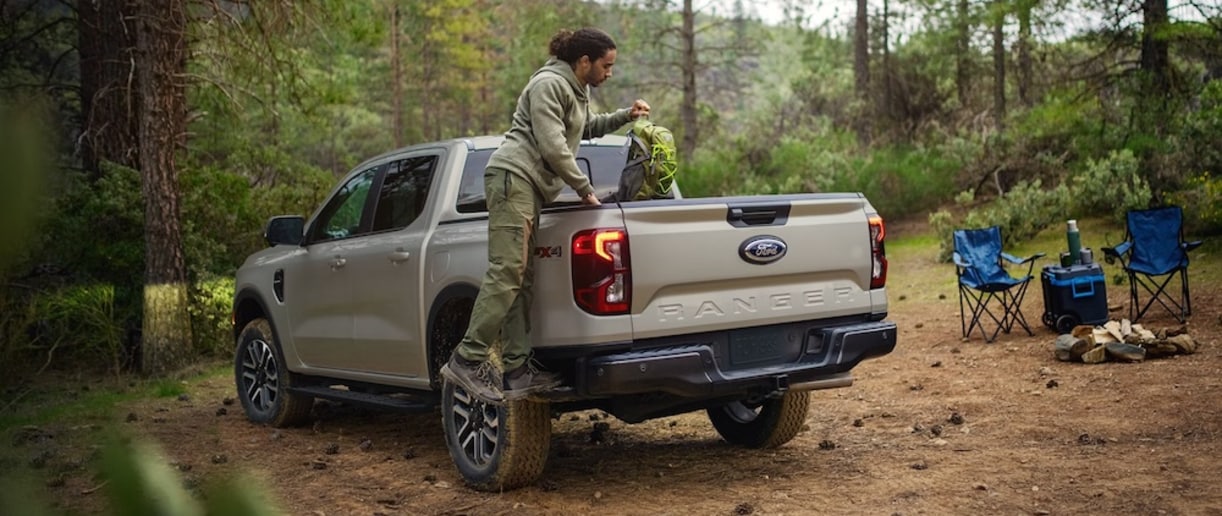 A person pulling a backpack out of the bed of a beige 2025 Ford Ranger pickup truck