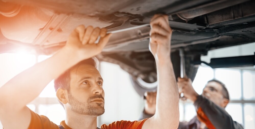 Two mechanics working on the undercarriage of an elevated vehicle