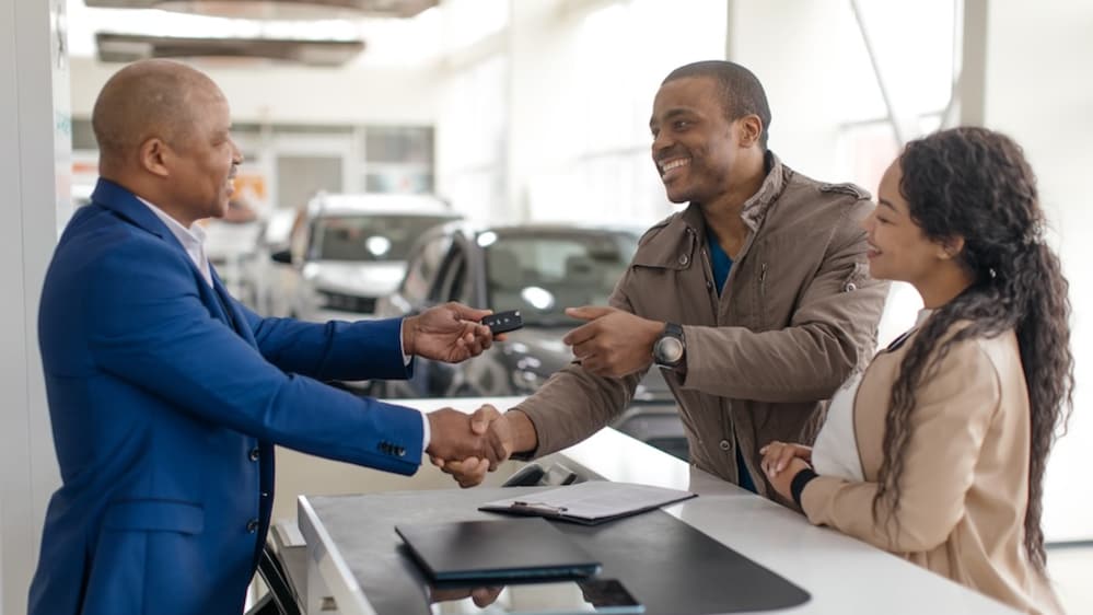 A couple shakes hands with a car salesman inside a car dealership