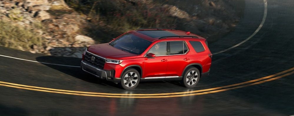 A red 2026 Honda Pilot SUV driving around the curve of a mountain road