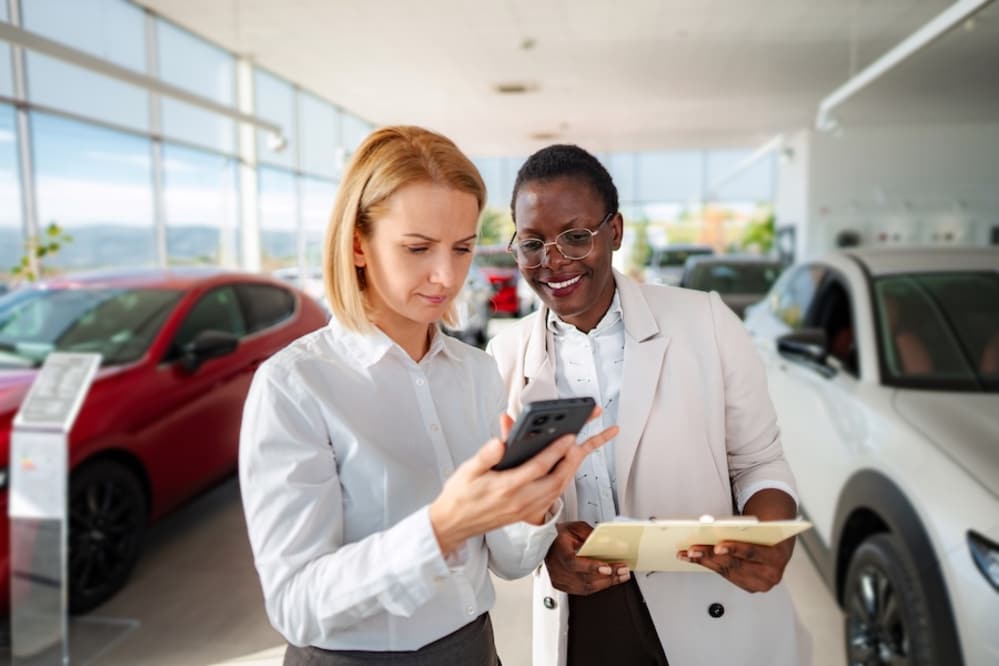 Two women looking at something on a phone inside a car dealership