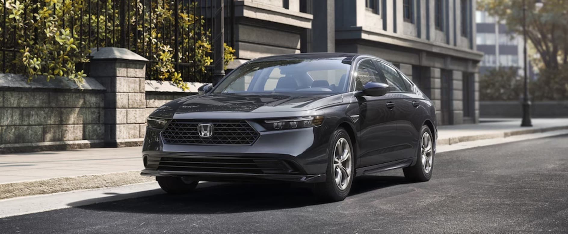 A gray 2026 Honda Accord sedan in a street in front of a stone building with an iron gate