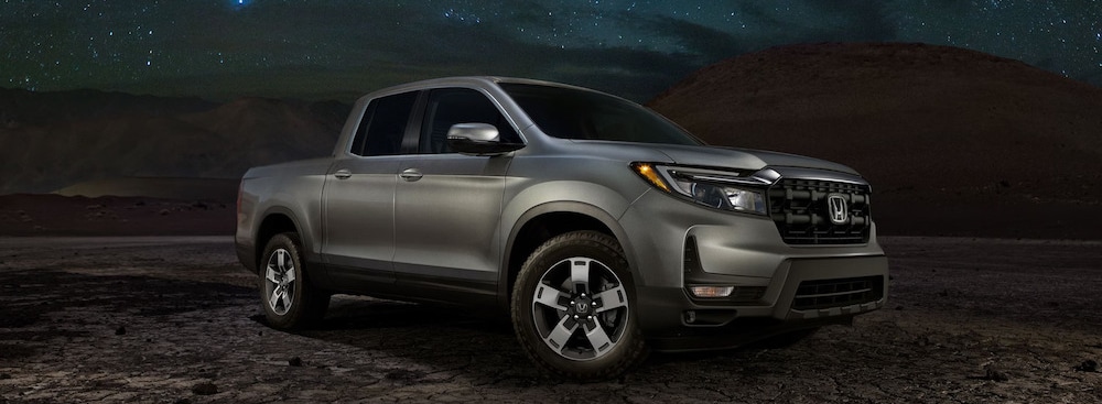 A silver 2026 Honda Ridgeline pickup parked near a mountain range, with the starry night sky in the background