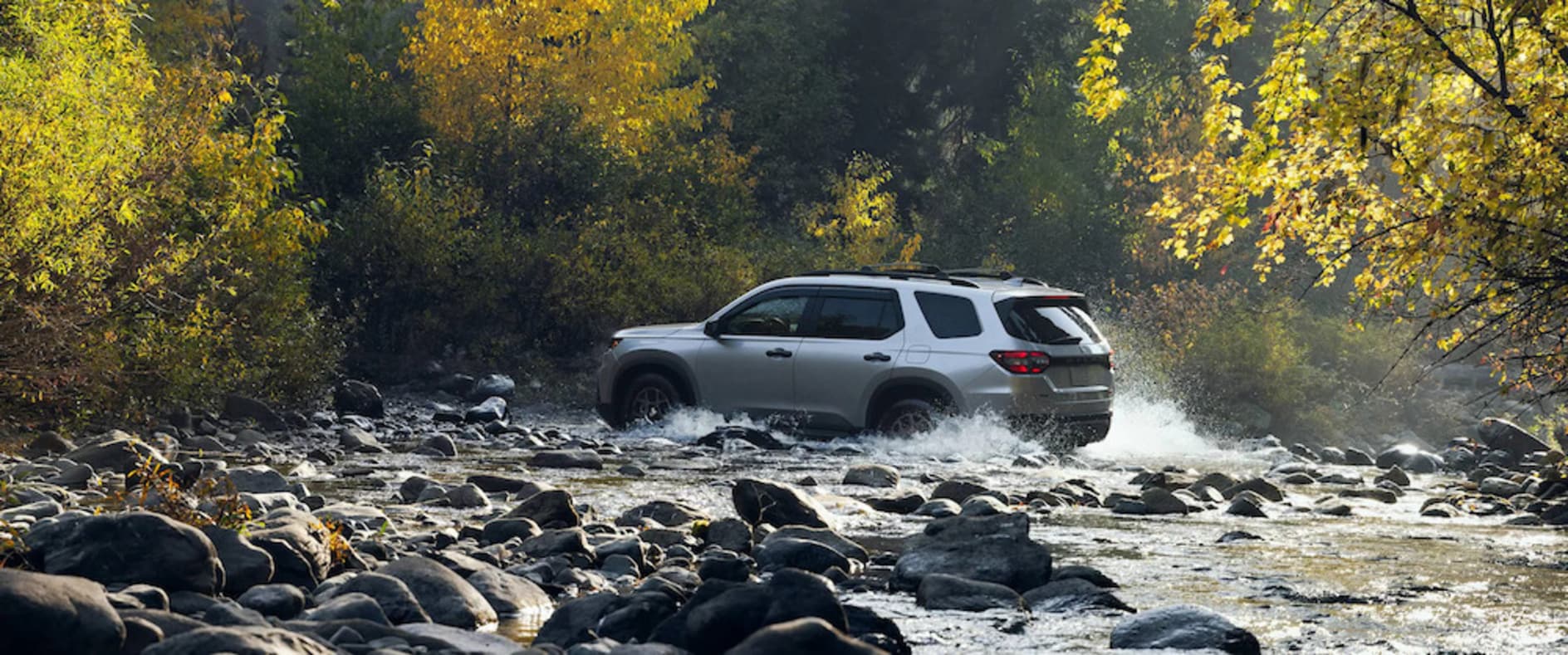 A silver 2025 Honda Pilot SUV driving out of a rocky riverbed
