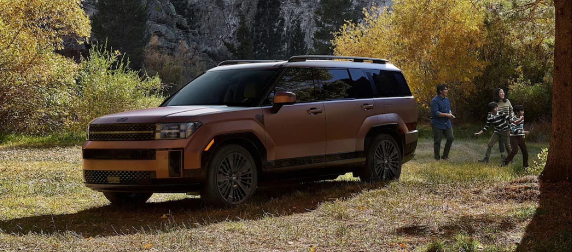 A copper-colored 2026 Hyundai Santa Fe SUV parked in a field, with a family playing together nearby