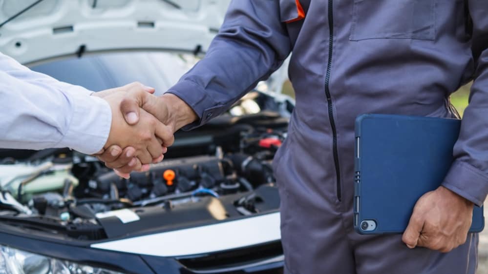 A service technician in blue coveralls shaking hands with a customer