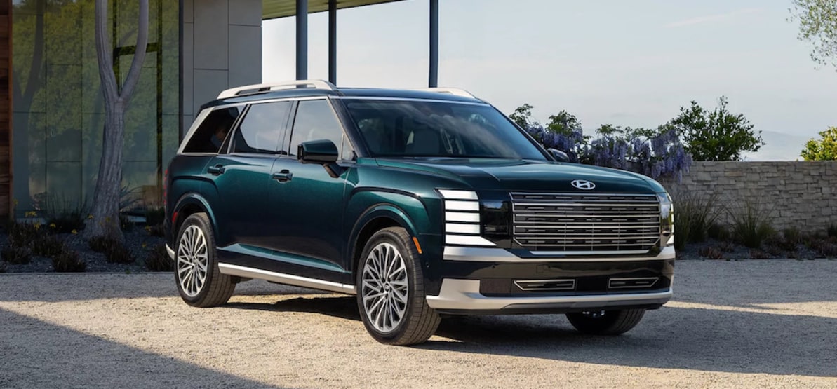 A dark green 2026 Hyundai Palisade parked on the gravel drive of a home