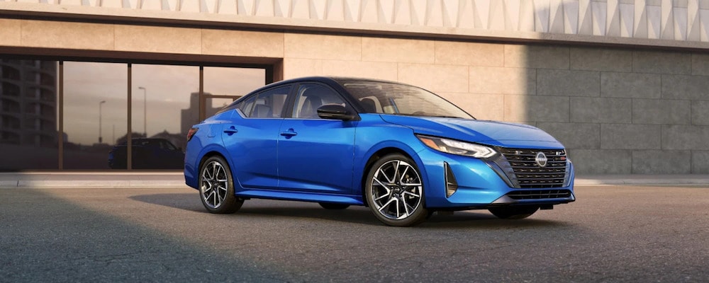 A bright blue 2025 Nissan Sentra sedan parked in front of a modern stone building