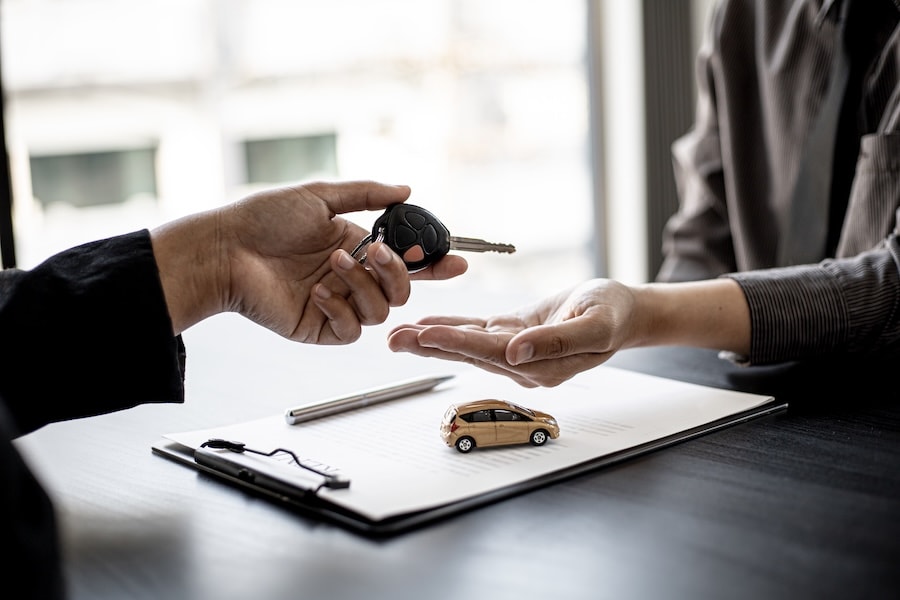 A car dealer handing a car key to a customer across a desk
