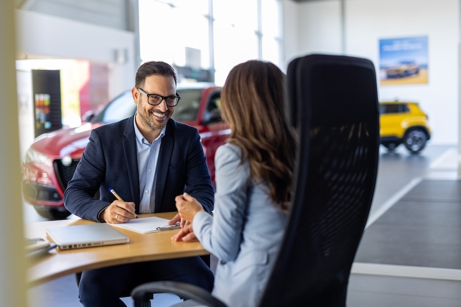 A car salesman discussing paperwork with a customer inside a car dealership