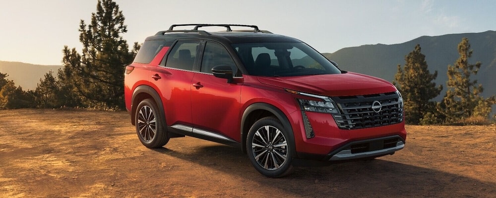 A red 2026 Nissan Pathfinder parked on a dirt ledge with pine trees and mountains in the background