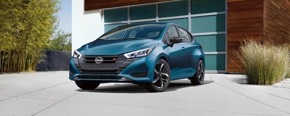 A turquoise 2025 Nissan Sentra sedan parked in the driveway of a modern glass-and-wood home, with a stand of bamboo in the background