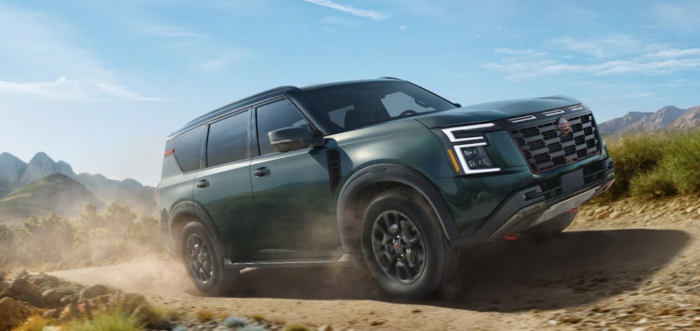 A dark green 2026 Nissan Armada SUV driving down a dusty trail with mountains in the background