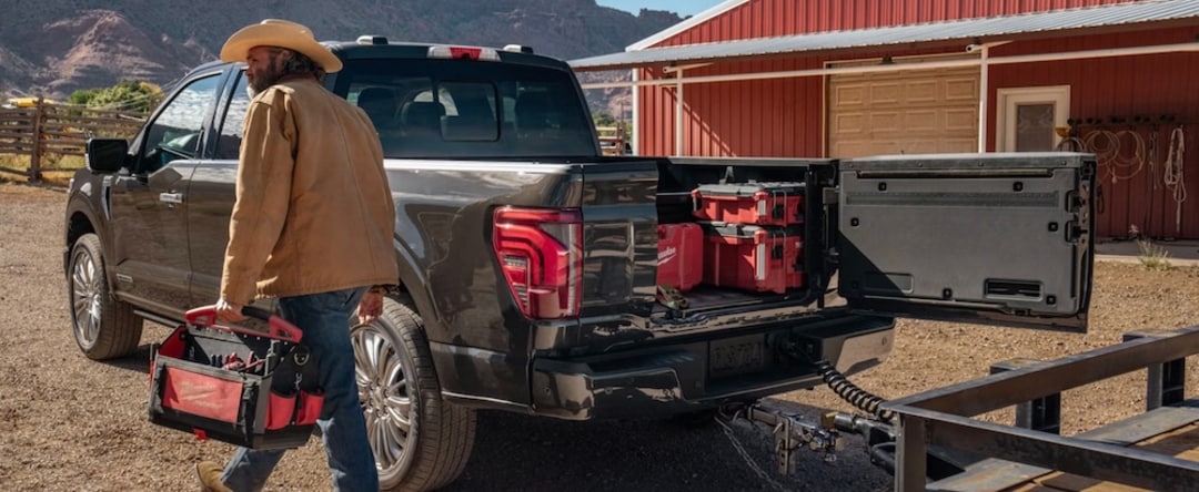 A person with a tool box walking beside a gray 2026 Ford F-150 pickup truck at a ranch