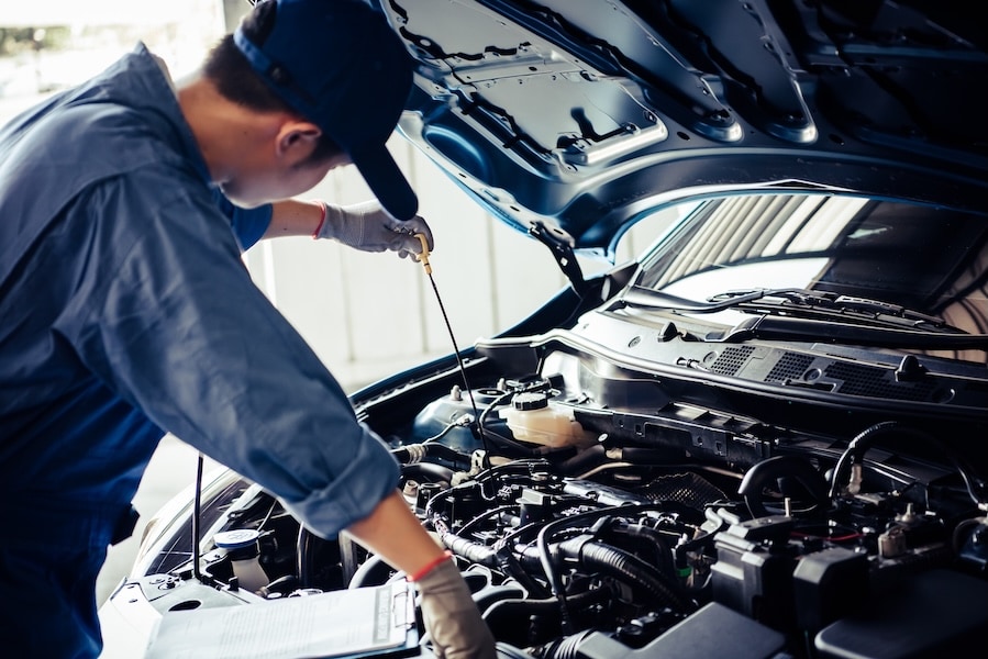 A person in blue coveralls and a baseball cap checking the engine oil level of a vehicle