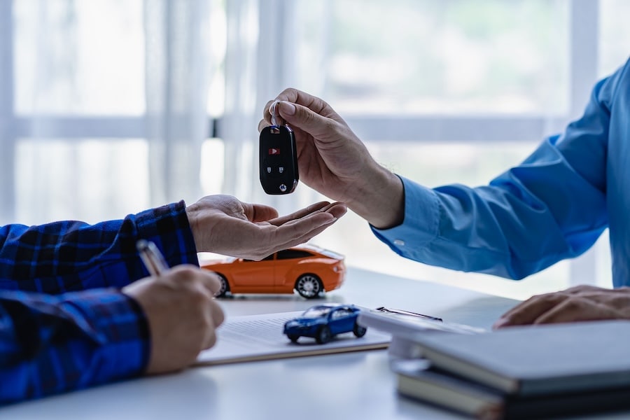 A car salesman handing a customer a car key across a desk