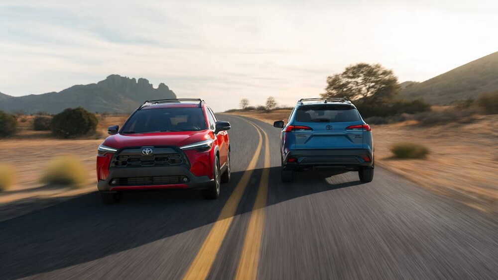 Two 2026 Toyota Corolla Cross SUVs, one red and the other blue, passing each other on a desert road