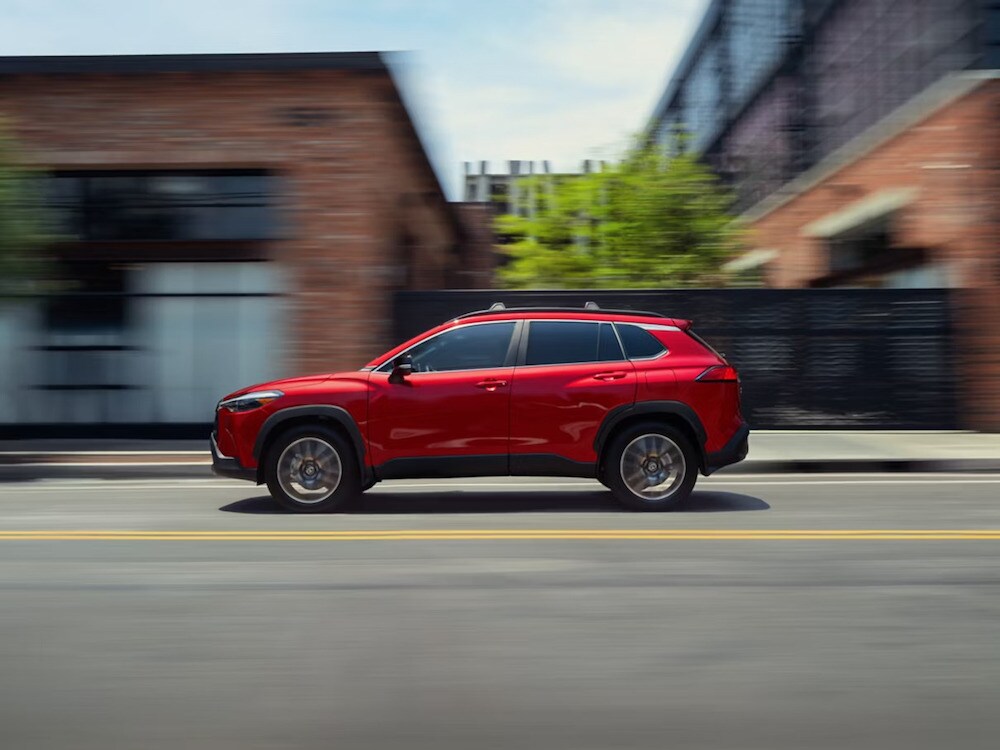 A red 2026 Toyota Corolla Cross SUV driving down a desert road