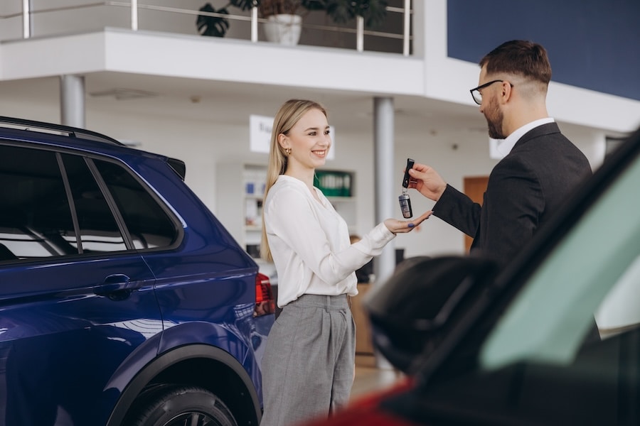 A car dealer handing a woman a car key, with a blue SUV behind her