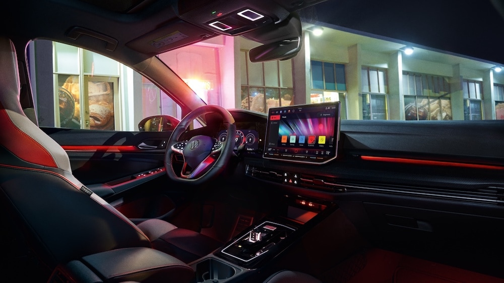 The steering wheel and dashboard of a 2025 Volkswagen Golf GTI, with a nighttime street visible through the windshield