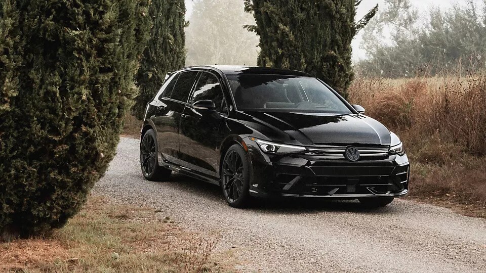 A black 2026 Volkswagen Golf R parked beside between hedges and dry grass