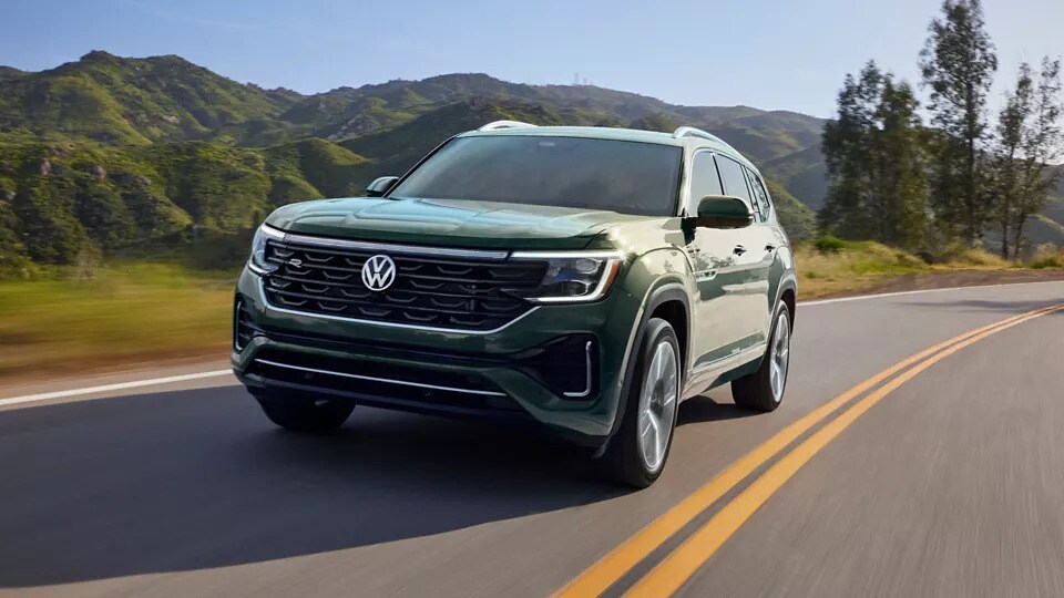 A green 2026 Volkswagen Atlas SUV driving down a road with mountains in the background