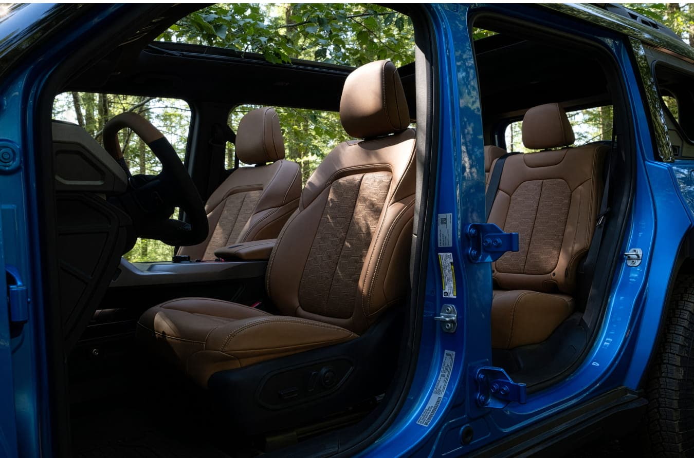 2026 Jeep Recon with doors open and revealing brown leather interior and seats, set against a leafy outdoor backdrop.